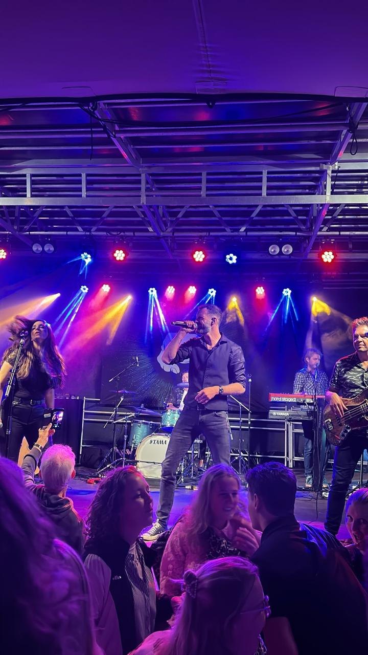 Zangeres en zanger van The Hits op een fel verlicht podium tijdens een openbaar optreden