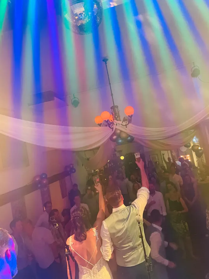 Bruidspaar heft het glas naar de dansende gasten op een bruiloftsfeest met feestverlichting en een discobal