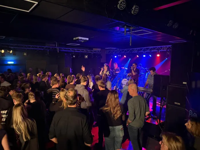 Coverband The Hits speelt op een verlicht podium voor een volle zaal tijdens een feestavond